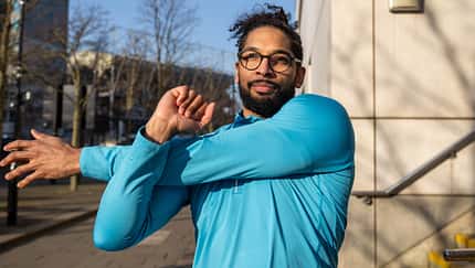 Ein Läufer mit Brille stretcht seine Arme.