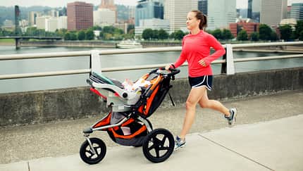 Junge Mutter läuft mit einem Baby im Laufkinderwagen Junge Mutter läuft mit einem Baby im Laufkinderwagen