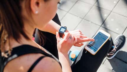 Eine Läuferin checkt ihre Gesundheitsdaten auf ihrer Uhr und in einer App.