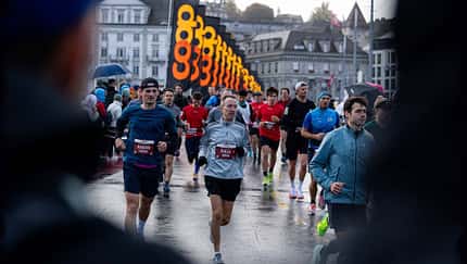 Läufer beim Marathon, verschwommen zwei Zuschauer in Regenjacken im Vordergrund. Läufer beim Marathon, verschwommen zwei Zuschauer in Regenjacken im Vordergrund.