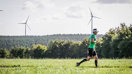 Ein Läufer umgeben von grüner Wiese, Wäldern und Windrädern im Hintergrund. Ein Läufer umgeben von grüner Wiese, Wäldern und Windrädern im Hintergrund.