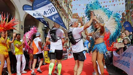 Läufer beim Zieleinlauf auf einem roten Teppich mit bunt verkleideten Tänzerinnen. Läufer beim Zieleinlauf auf einem roten Teppich mit bunt verkleideten Tänzerinnen.