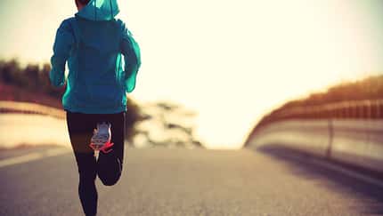 Ambitionierte Läuferin beim Lauftraining auf einer Straße im Sonnenaufgang
