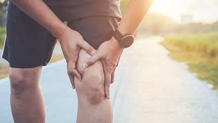 Injury from workout concept : Asian man use hands hold on his knee while running on road in the park. Shot in morning time, sunlight and warm effect with copy space for text or design