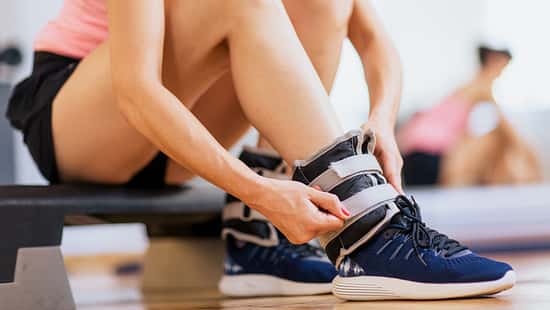 Eine Sportlerin befestigt Gewichtsmanschetten an ihren Fußgelenken.