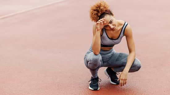 Red-S-Syndrom: Energiedefizit im Sport. Eine erschöpfte Läuferin hockt auf einer Laufbahn.