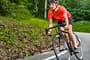 Eine junge Frau fährt Rennrad auf einer Straße durch den Wald. Triathlon-Trainingsplan: Olympische Distanz schaffen.