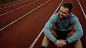 Caucasian male athlete smiling crouching down sitting on tracking field