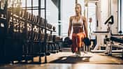Female athlete exercising with dumbbells in a lunge position at gym.