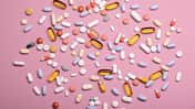 Top view of spoon with various pills and tablets on the pink background