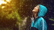 Laufmotivation bei jedem Wetter: Junge Läuferin steht mit einer Regenjacke glücklich im Regen.