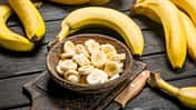Bananas and banana pieces in a wooden plate on a cutting Board with a knife.