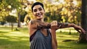 Sport mit Tattoo: Junge Frau mit Tätowierung dehnt sich nach dem Joggen.