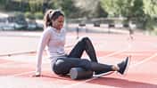 Regeneration im Lauftraining: Eine Läuferin rollt ihre Beinmuskulatur auf einer Faszienrolle aus.