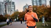 Happy sportswoman with earbuds running in the park.