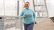 Glückliche Plus-Size-Läuferin läuft auf einer Brücke.
