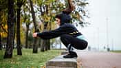 Tabata-Intervalle: Eine Läuferin macht Box-Jumps auf einer Bank im Park.