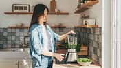 Eine Frau mixt sich mit einem Smoothiemaker einen grünen Smoothie.