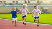 Drei Kinder laufen zusammen auf einer Laufbahn im Stadion.