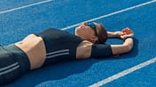 Overreaching vs. Übertraining: Eine erschöpfte Läuferin liegt auf einer blauen Tartanlaufbahn.