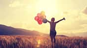 cheering young asian woman on grassland with colored balloons